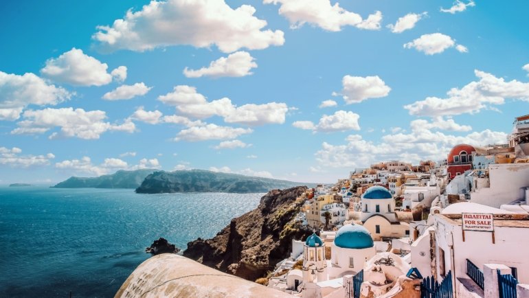 A stunning view of the iconic whitewashed village of Oia in Santorini, one of the best places to visit in Greece, with its blue-domed churches overlooking the Aegean Sea.