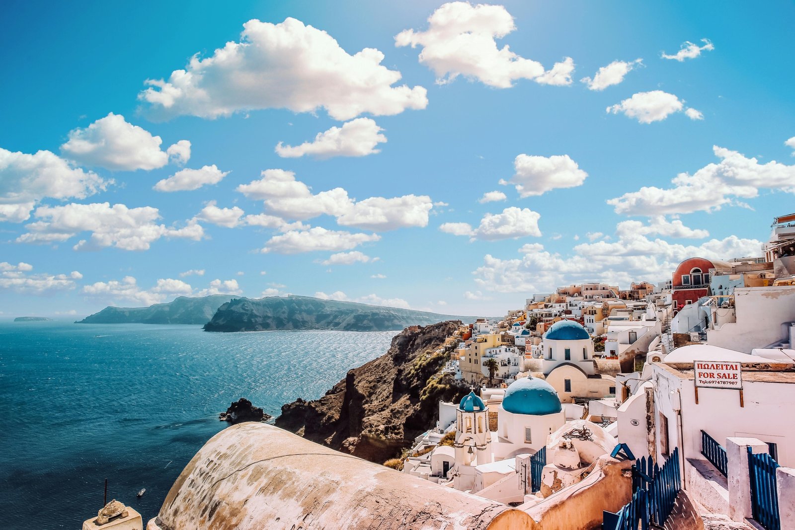 A stunning view of the iconic whitewashed village of Oia in Santorini, one of the best places to visit in Greece, with its blue-domed churches overlooking the Aegean Sea.