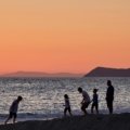 A happy family with young children walking hand-in-hand on a sunny beach, enjoying their family trip to Greece.