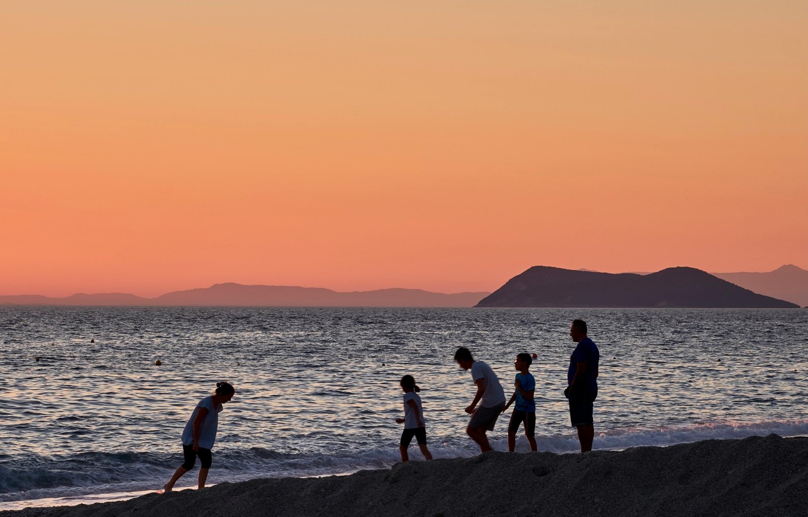 A happy family with young children walking hand-in-hand on a sunny beach, enjoying their family trip to Greece.