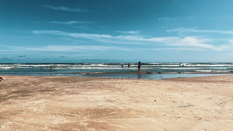 A wide, sandy Texas beach on a sunny day with gentle waves from the Gulf of Mexico, an ideal vacation spot.