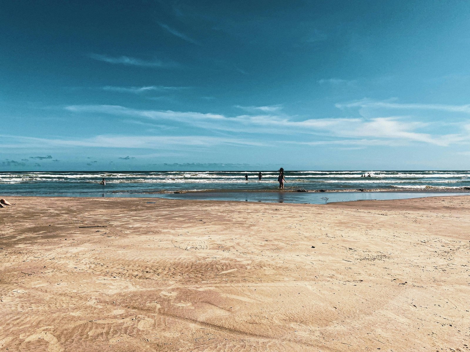 A wide, sandy Texas beach on a sunny day with gentle waves from the Gulf of Mexico, an ideal vacation spot.
