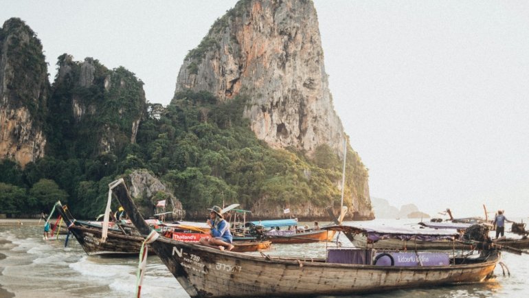 A stunning view of traditional longtail boats in a turquoise bay, an iconic destination for travelers deciding where to go in Thailand for beautiful beaches and adventure.