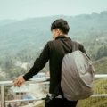 A young backpacker on a budget travel adventure looks out over a stunning mountain valley, an example of exploring one of the world's cheapest places to travel.