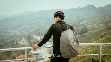 A young backpacker on a budget travel adventure looks out over a stunning mountain valley, an example of exploring one of the world's cheapest places to travel.