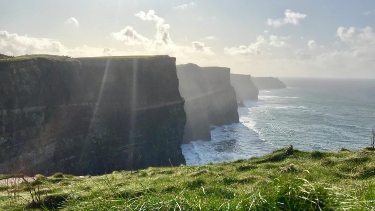 A stunning, wide-angle view of the iconic Cliffs of Moher, a key destination for planning a first trip to Ireland.