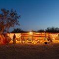 A traditional Berber desert camp for camping in the Sahara, with tents lit up under a starry night sky and a warm campfire in the foreground.
