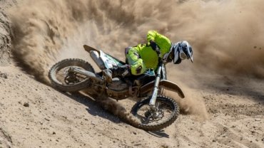 Desert Gateway Dirt Bike Tours: An exhilarating off-road adventure with a rider on a dirt bike, speeding through vast desert dunes and canyons, wearing full safety gear.