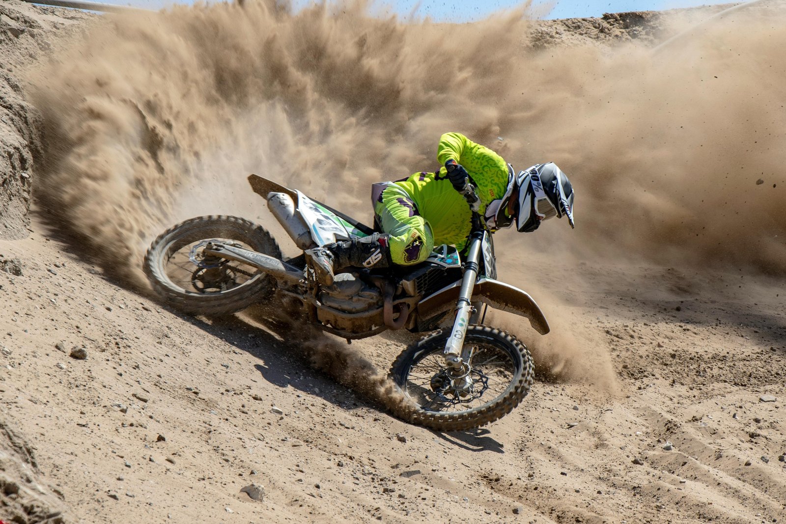 Desert Gateway Dirt Bike Tours: An exhilarating off-road adventure with a rider on a dirt bike, speeding through vast desert dunes and canyons, wearing full safety gear.
