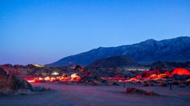 A traditional Sahara desert camp in Morocco at night, with glowing tents and a campfire under a brilliant starry sky over the dunes.
