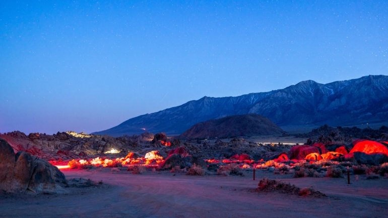 A traditional Sahara desert camp in Morocco at night, with glowing tents and a campfire under a brilliant starry sky over the dunes.