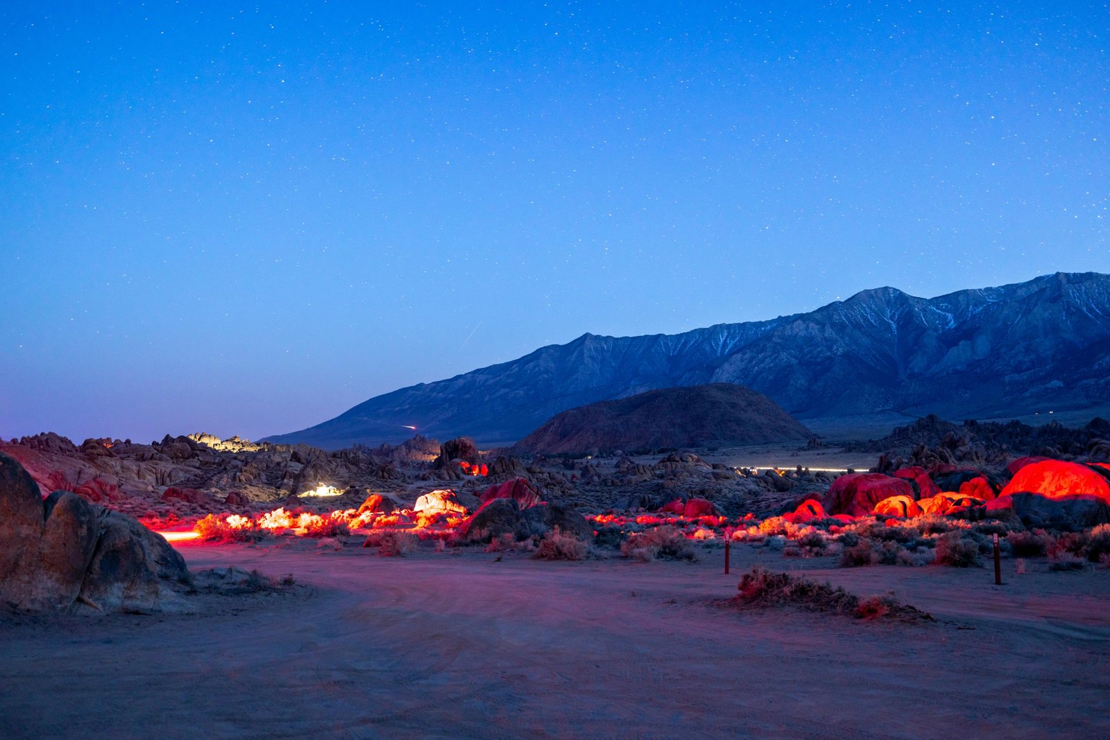 A traditional Sahara desert camp in Morocco at night, with glowing tents and a campfire under a brilliant starry sky over the dunes.