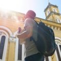 A traveler with a backpack overlooks a historic cityscape, representing one of the best places to travel cheap in Europe.