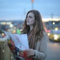 A young person happily plans their route with a map for a budget-friendly road trip to cheap travel spots in the US.