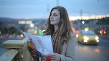 A young person happily plans their route with a map for a budget-friendly road trip to cheap travel spots in the US.
