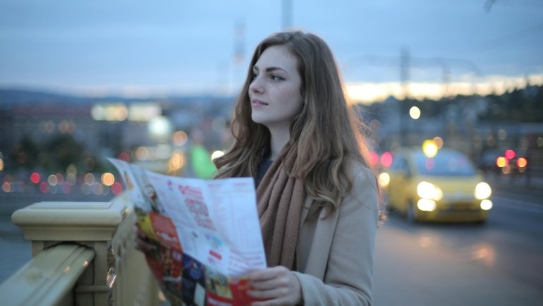 A young person happily plans their route with a map for a budget-friendly road trip to cheap travel spots in the US.