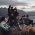 A diverse group of solo travelers laughing together on a scenic viewpoint during a singles vacation group tour.