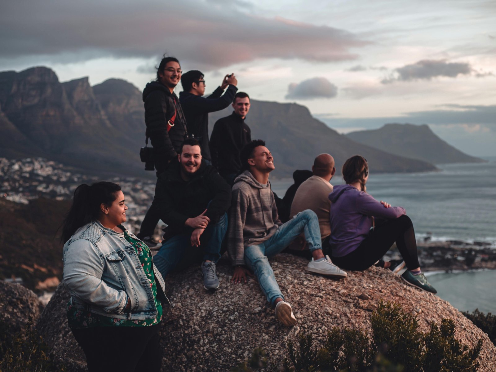 A group of happy friends on a holidays for singles over 40 Australia tour, laughing together with a beautiful coastal landscape in the background.