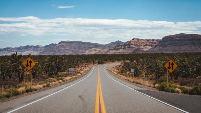 A scenic view of a car on an open road heading towards mountains, illustrating the adventure of finding the best places to travel in the US.