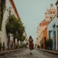 Solo traveler with a small backpack exploring a picturesque cobblestone street in a historic European city, representing freedom and safety for independent adventures.