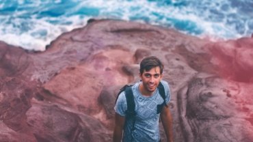 A young traveler with a backpack looks out over a scenic landscape, representing the joy of discovering cheap places to see and traveling on a budget.