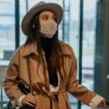 A stylish traveler, possibly a woman, effortlessly carrying a 21 cm compact travel hat box with her luggage at an airport, symbolizing protection for hats like fascinators or fedoras and adding a touch of vintage elegance to her journey.