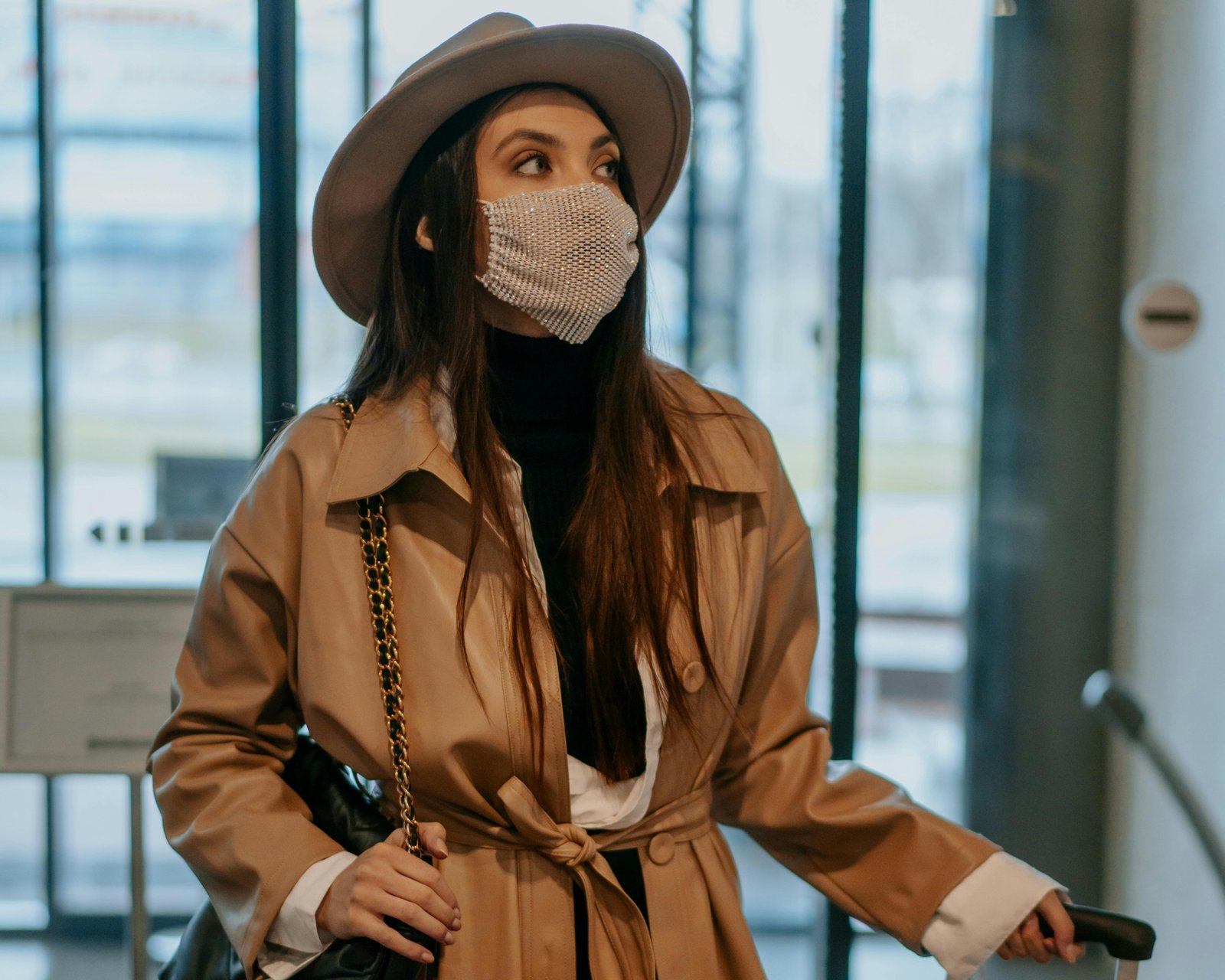 A stylish traveler, possibly a woman, effortlessly carrying a 21 cm compact travel hat box with her luggage at an airport, symbolizing protection for hats like fascinators or fedoras and adding a touch of vintage elegance to her journey.