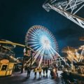 A vibrant night view of the Wildwood Boardwalk, with the brightly lit amusement rides and the iconic Ferris wheel of Morey's Piers illuminating the Jersey Shore.