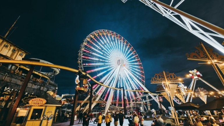 A vibrant night view of the Wildwood Boardwalk, with the brightly lit amusement rides and the iconic Ferris wheel of Morey's Piers illuminating the Jersey Shore.