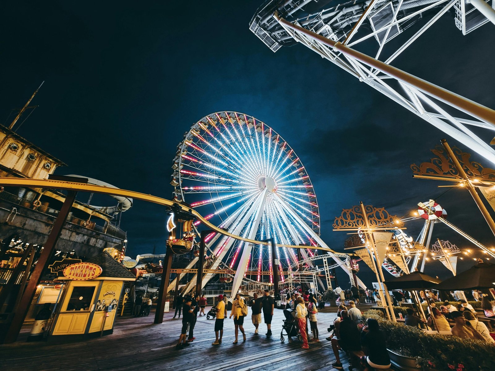 A vibrant night view of the Wildwood Boardwalk, with the brightly lit amusement rides and the iconic Ferris wheel of Morey's Piers illuminating the Jersey Shore.