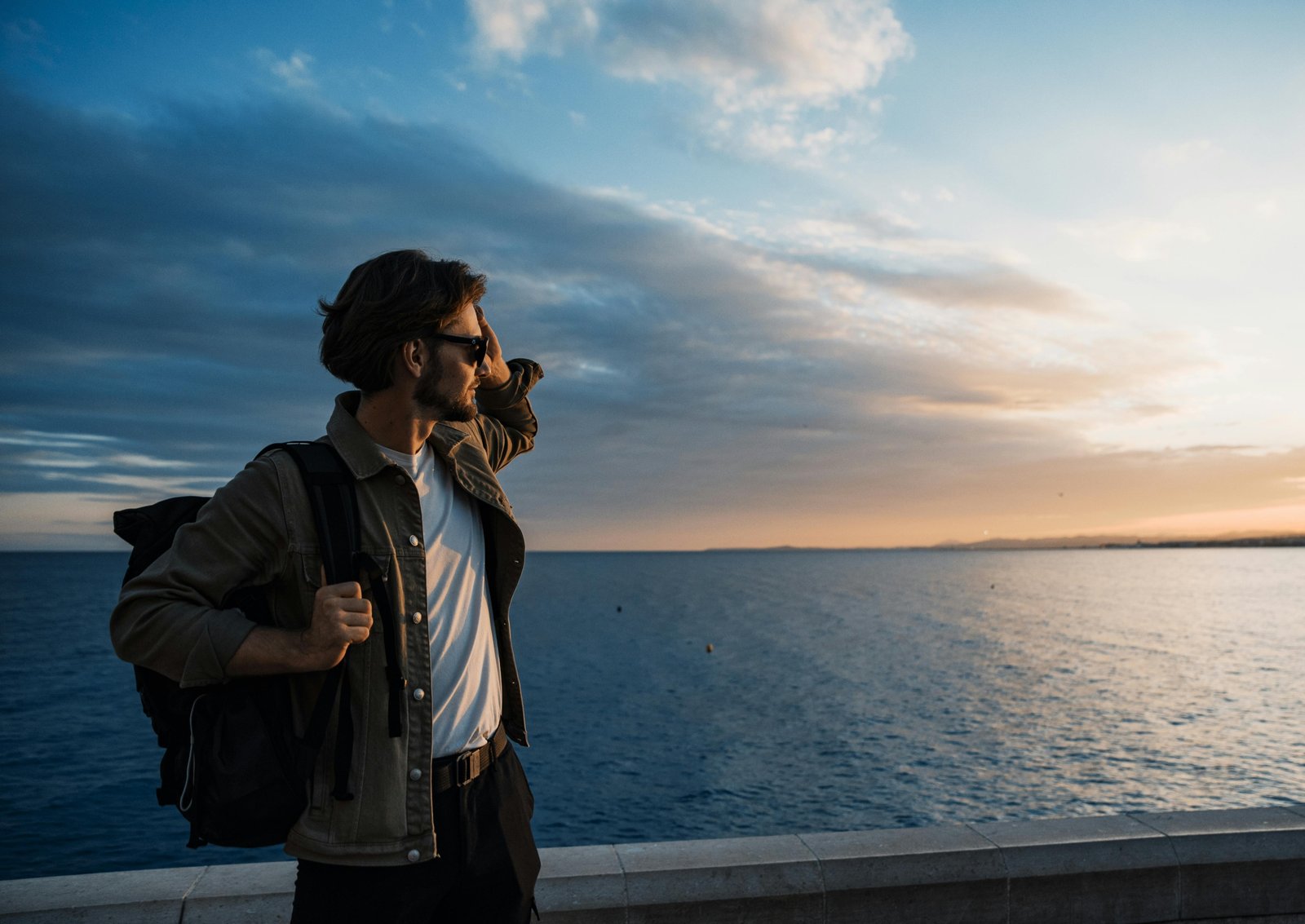 A young traveler with a backpack looks out over a scenic mountain vista, an example of an affordable and authentic experience made possible by budget travel strategies.