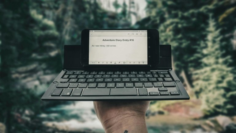 A digital nomad typing on a compact travel keyboard with a tablet, highlighting portable productivity and remote work flexibility in a travel setting.