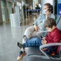 Happy family (parents and child) effortlessly navigating an airport with a lightweight, FAA-approved Cosco Scenera NEXT travel car seat, highlighting stress-free and safe family adventures.