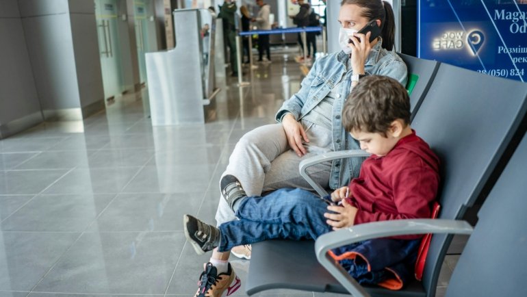Happy family (parents and child) effortlessly navigating an airport with a lightweight, FAA-approved Cosco Scenera NEXT travel car seat, highlighting stress-free and safe family adventures.