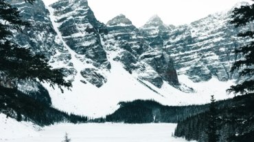 A stunning Canadian winter wonderland scene with pristine snow covering majestic mountains and evergreen forests under a bright, crisp sky, symbolizing the magic and adventure of Canadian winter travel. This image is ideal for articles on essential Canadian winter travel advice, packing tips, and winter activities.