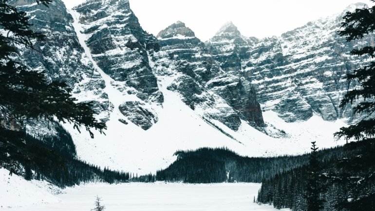 A stunning Canadian winter wonderland scene with pristine snow covering majestic mountains and evergreen forests under a bright, crisp sky, symbolizing the magic and adventure of Canadian winter travel. This image is ideal for articles on essential Canadian winter travel advice, packing tips, and winter activities.