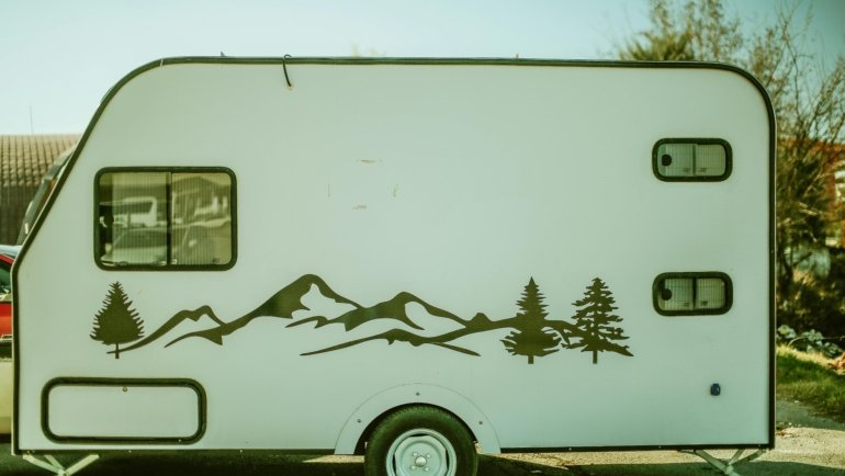 A sleek lightweight travel trailer, such as a compact teardrop or small fiberglass camper, parked in a picturesque natural setting like a mountain vista or forest campground, symbolizing accessible road trip adventures and easy outdoor living for modern explorers.