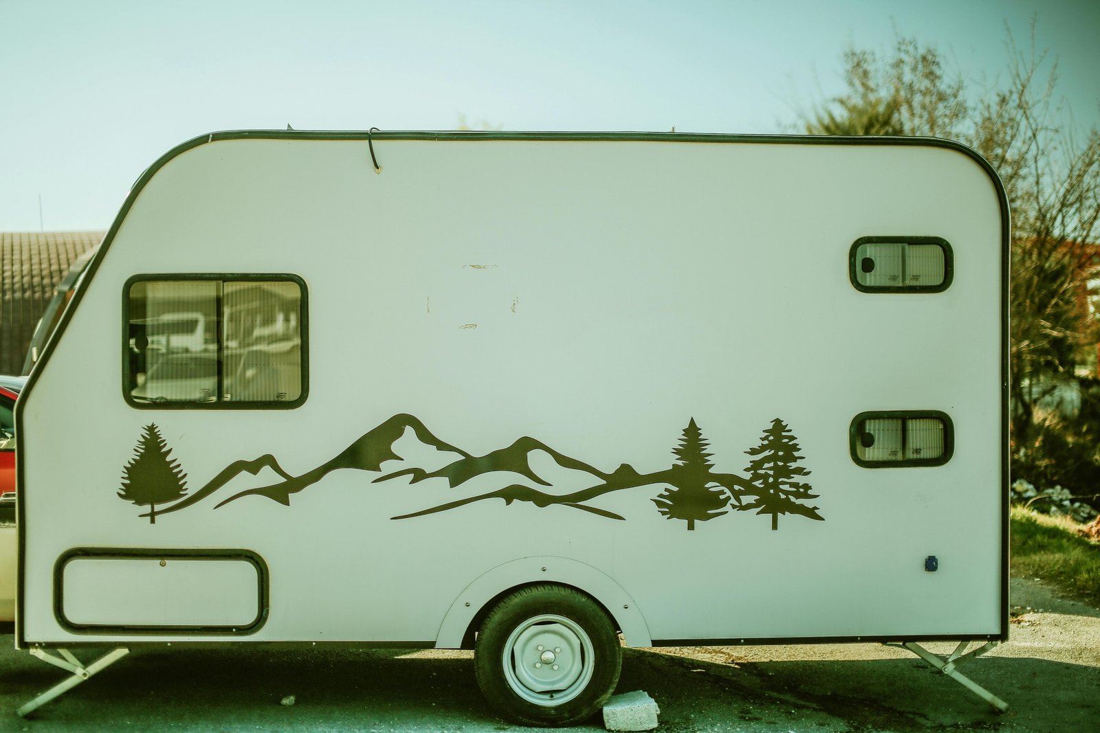 A sleek lightweight travel trailer, such as a compact teardrop or small fiberglass camper, parked in a picturesque natural setting like a mountain vista or forest campground, symbolizing accessible road trip adventures and easy outdoor living for modern explorers.