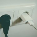 A hand plugging a universal travel adapter into a Type F European power socket, with a smartphone charging, illustrating safe and essential electronics charging for trips to Spain.