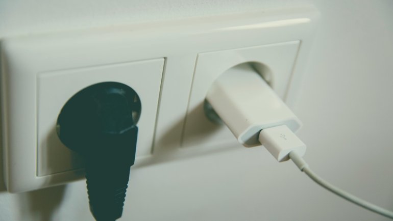 A hand plugging a universal travel adapter into a Type F European power socket, with a smartphone charging, illustrating safe and essential electronics charging for trips to Spain.