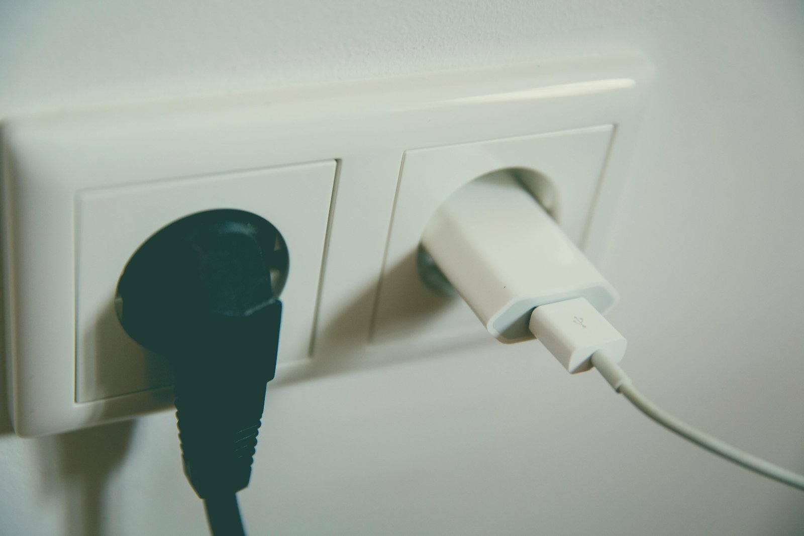 A hand plugging a universal travel adapter into a Type F European power socket, with a smartphone charging, illustrating safe and essential electronics charging for trips to Spain.