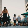 A parent confidently pushes a modern Zoe Traveler stroller with a happy baby through a busy airport terminal, showcasing its lightweight and compact design for convenient family travel.