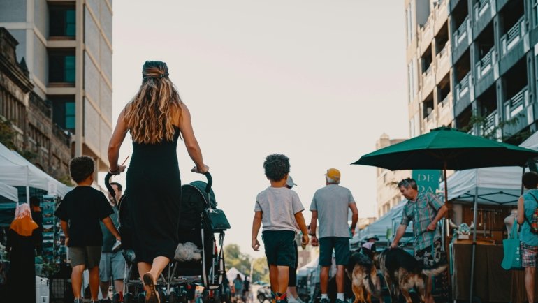 A parent confidently pushes a modern Zoe Traveler stroller with a happy baby through a busy airport terminal, showcasing its lightweight and compact design for convenient family travel.