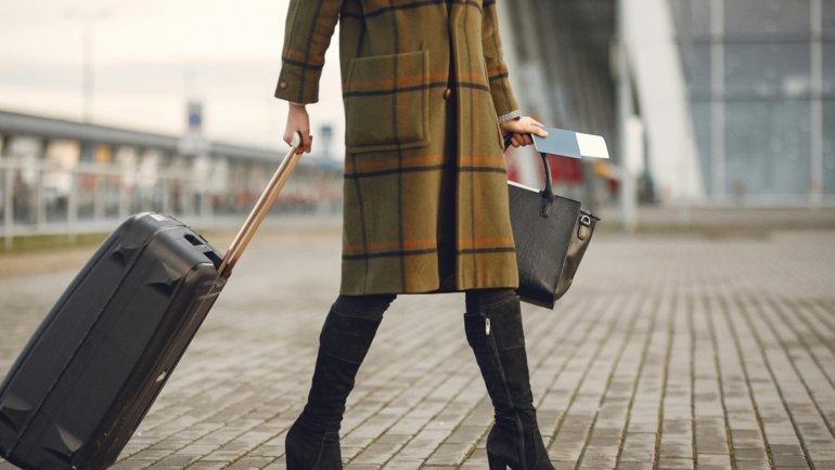 A traveler confidently walking with a sleek, black spinner cabin bag through a bright, modern airport terminal, illustrating the benefits of the best carry-on luggage for smooth journeys.