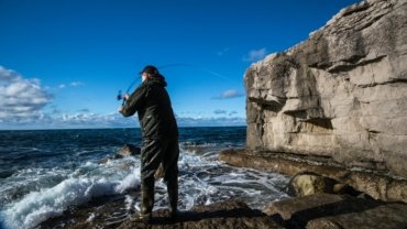 Adventurous angler with a portable travel fishing rod and backpack enjoying fishing in a scenic natural landscape, highlighting convenience for travel.
