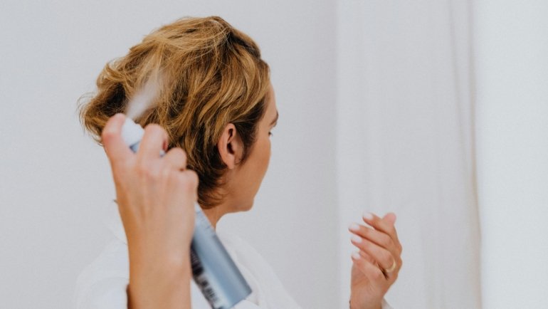 Confident woman using a travel size hairspray to perfect her hairstyle while traveling, showcasing beauty on the go.
