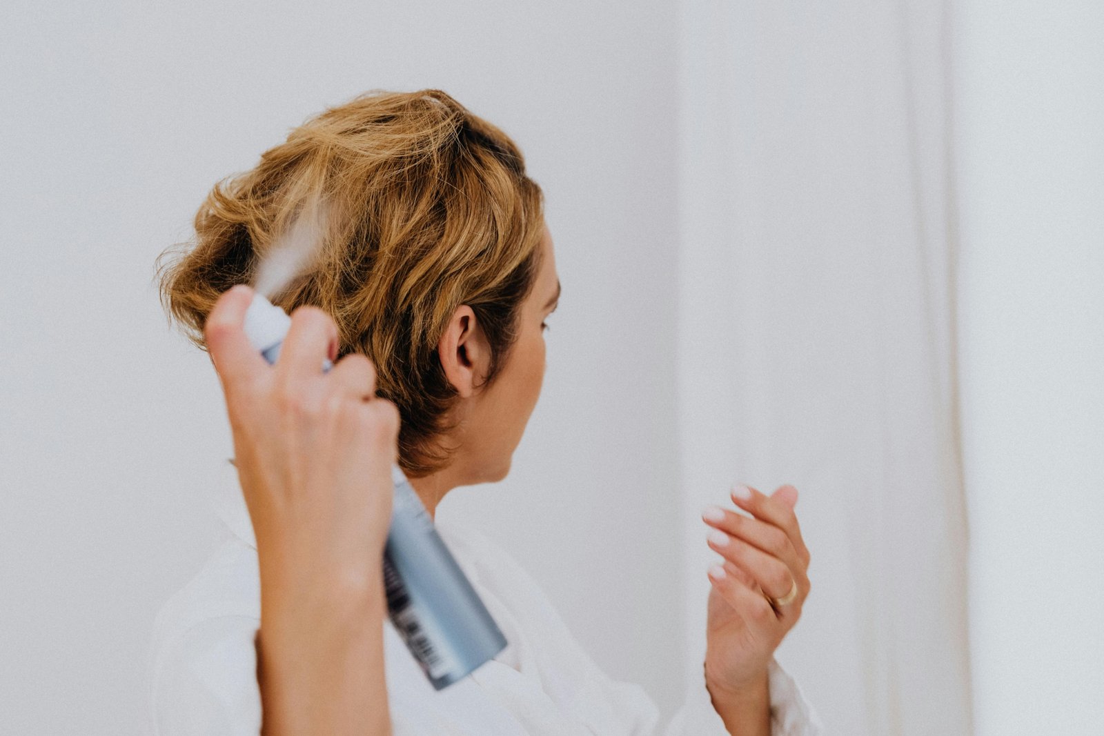 Confident woman using a travel size hairspray to perfect her hairstyle while traveling, showcasing beauty on the go.
