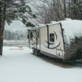 Hands working to winterize a travel trailer's plumbing system with RV antifreeze, protecting it from winter damage.