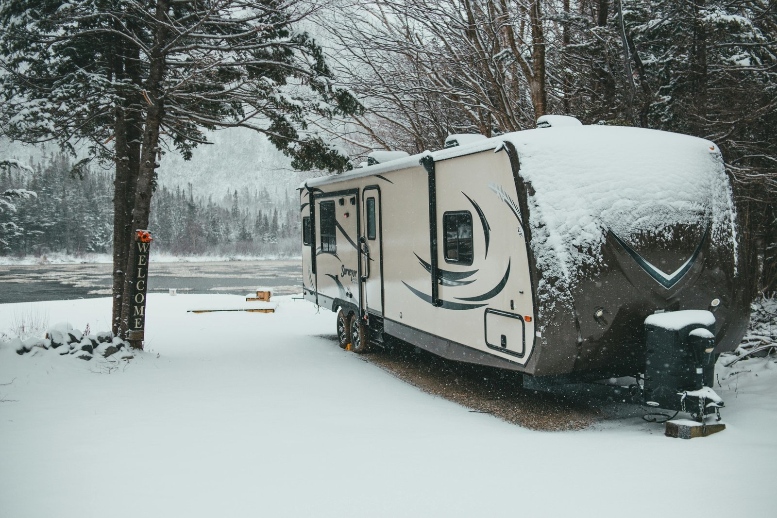 Hands working to winterize a travel trailer's plumbing system with RV antifreeze, protecting it from winter damage.