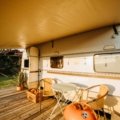 Travel trailer toy hauler with open ramp patio, showing an ATV and people enjoying a scenic outdoor adventure, highlighting versatile RV living.